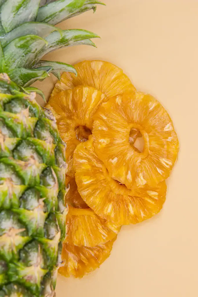 Getrocknete Ananasringe neben ganzer Ananas vor orangenem Hintergrund
